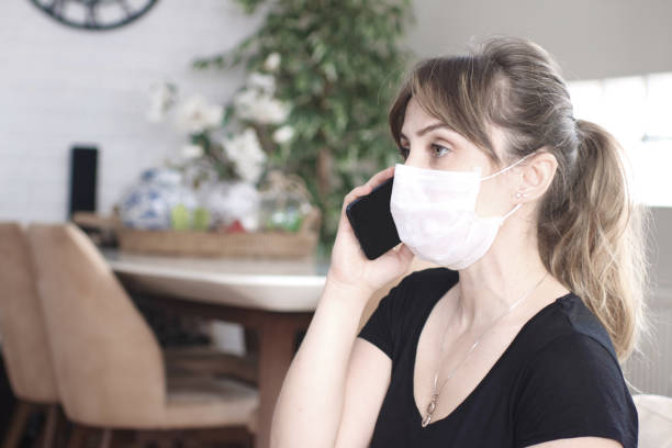 istock Woman wearing a protective face mask and using a mobile phone at home 1222135213