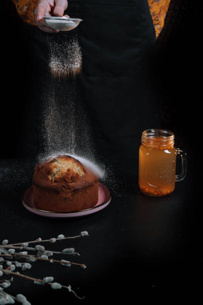istock Female hands in an orange dress sprinkle Easter cake with icing sugar on a dark background. 1222140811