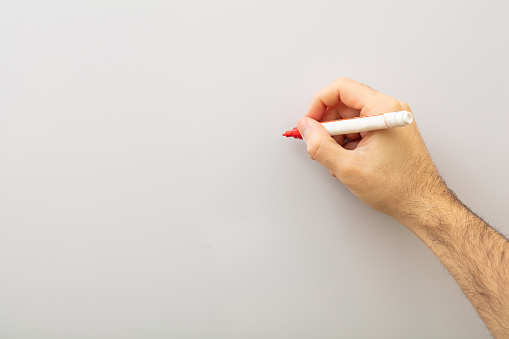 Hand with a marker isolated on gray background. Man holding a red marker against whiteboard, copy space