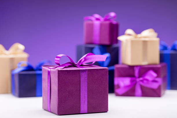 Present. Gift boxes in multicolored paper with lilac ribbons, on purple background. Happy Holidays.