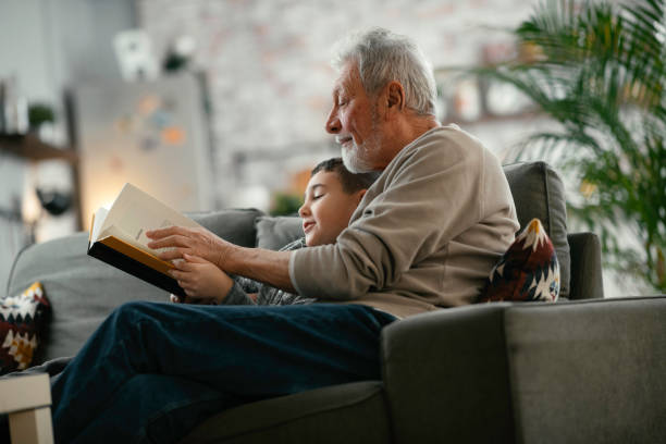 grand-père et petit-fils lecture livre ensemble. - grandparent family reading inside of photos et images de collection