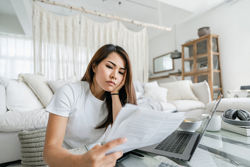 Estresada y preocupada joven asiática trabajando desde casa, manejando papeles y revisando sus finanzas photo