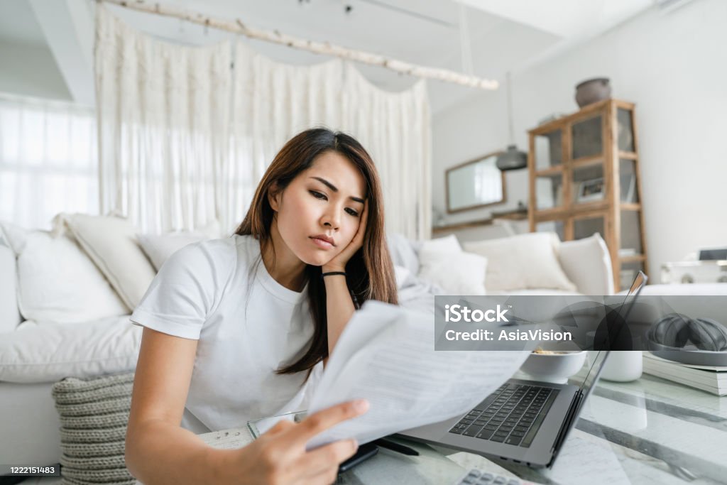 Stressed and worried young Asian woman working from home, handling paperworks and going through her financials Financial Bill Stock Photo