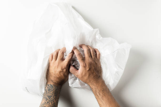 istock Man hand with tattoos squeezing a crumpled foam sheet isolated on white background. 1222157583