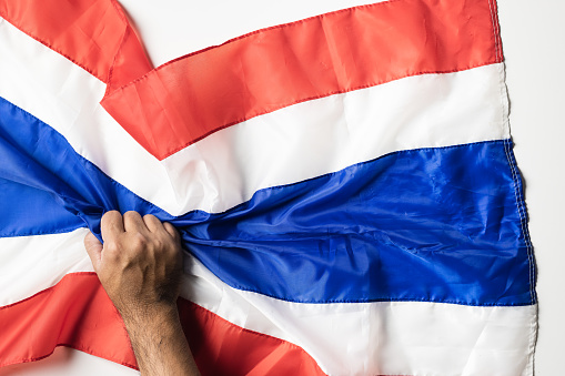 Man hand with tattoos holding Thailand Flag Wrinkled On white Background for copy space.