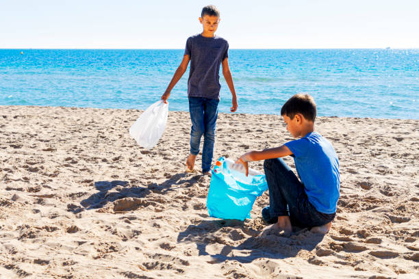istock Volunteers cleaning beach from plastic. Boys walking on the beach and picking up plastic bottles trash and putting into plastic bag for recycle 1222158638