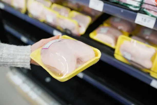 Photo of Woman choosing packed chicken meat in supermarket