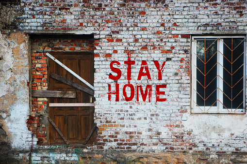 Stay home inscription on old brick wall .sealed door and barred window. Self-isolation at home from a coronovirus concept.