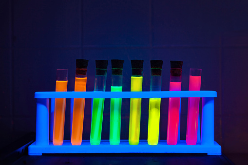 Three ml beakers with colored liquids in them shot under colored lights.