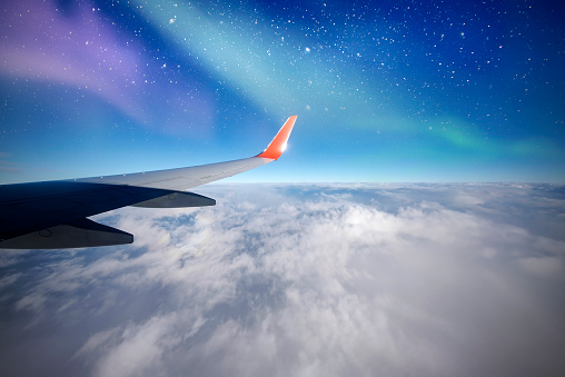 Plane over north, Aurora or northern lights from airplane window, Aurora Borealis, night sky with clouds and stars