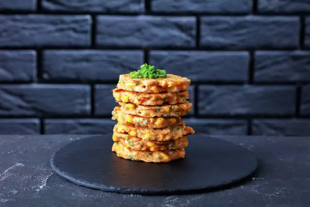 stack of cheese and corn pancakes on a black stone plate on a concrete table with a brick wall at the background, horizontal view from above,