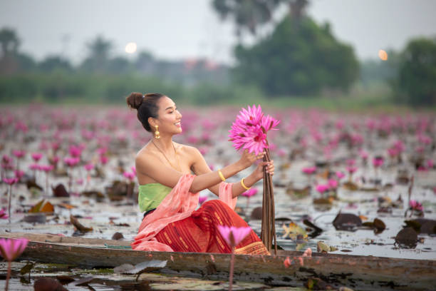 Young Asian women in Traditional dress in the boat and pink lotus flowers in the pond.Beautiful girls in traditional costume.Thai girl in retro Thai dress, Thai girl in traditional dress costume Portrait beautiful woman in local costume on the wooden boat in the lake of pink lotus blossom in Thailand. udon thani stock pictures, royalty-free photos & images