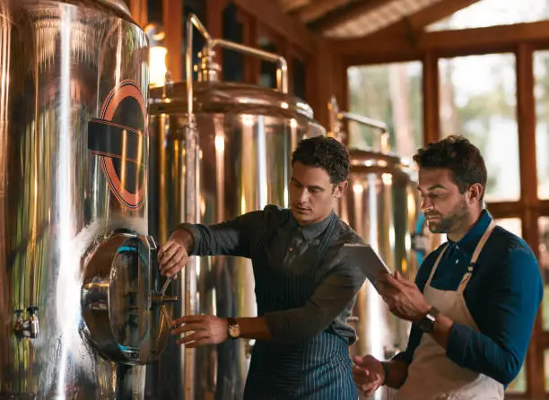 Shot of two young working men doing inspection of their beer making machinery inside of a beer brewery during the day