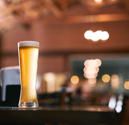 Shot of a glass of beer standing on its own at a table  inside of a beer brewery during the day