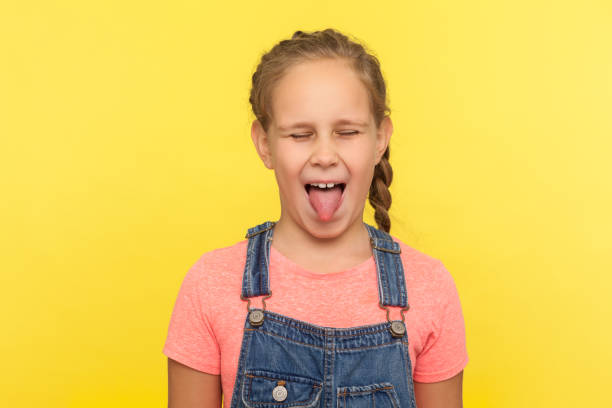 porträt von freche kleine mädchen in jeans overalls herausragen zunge und halten die augen geschlossen, ungehorsam kind - child bizarre little girls humor stock-fotos und bilder