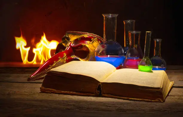 Medieval alchemy and pharmacy concept with old book, traditional mask and bottles with medicine. Text in the book is not recognizible.