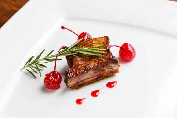 istock Grilled pork ribs decorated with rosemary and caramelized cherry served on a white plate 1222171108