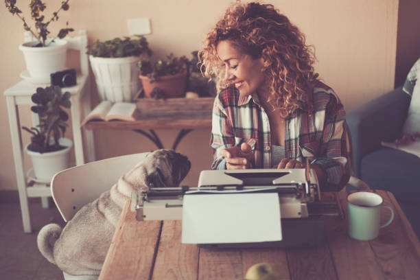 istock Cheerful beautiful woman with her lovely dog pug at home while write for work with old typewriter and enjoy the indoor leisure activity with cup of tea - concept of job and best friend animal 1222173937