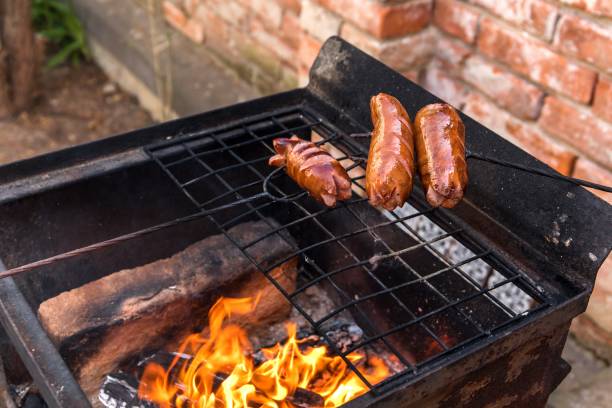 istock Sausage stabbed on an iron fork and toasted over an fire. Old rusty metal grill. Burning logs in a barbecue grill. 1222176632