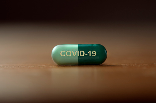 A pill with the text covid-19 printed on it on a wooden table