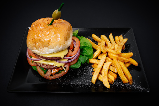 Tasty cheeseburgers or hamburgers on wooden tray, some seasonings and cutlery near it.