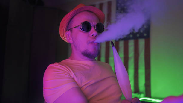 kuvapankkikuvat ja rojaltivapaat kuvat aiheesta hipster hengittää savupilveä polttaen hookahia neonvaloissa - electronic hookah smoke