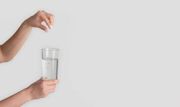 istock Unrecognizable woman adding pill into glass of water on light background, closeup. Empty space 1222187637