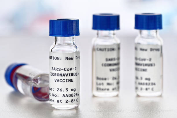 istock Coronavirus sars-CoV-2 vaccine concept, small vials with blue caps on white desk (Sticker is own design with dummy data - not a real product) 1222187930