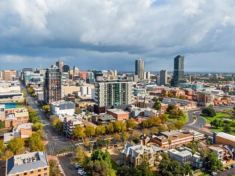 Wide angle view as storm clouds gather over the city of Adelaide, a city in isolation from the coronavirus. Some cars are visible, but the streets are mostly empty in this aerial view captured on the East Side of the city looking northwest. The trees have some autumn colours as winter approaches.