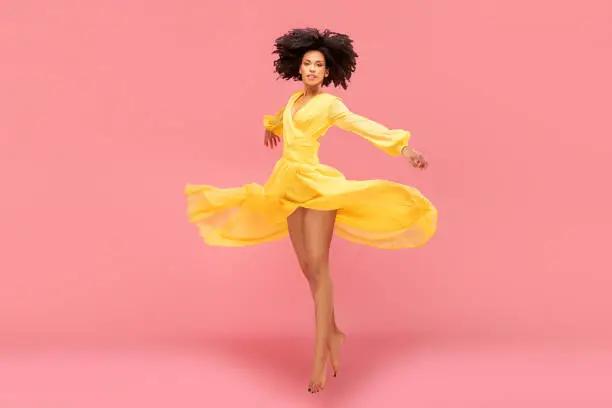 Photo of Afro girl dancing in yellow maxi dress.