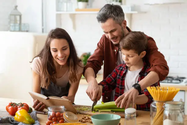 Photo of Mother, father, son chopping vegetables on kitchen