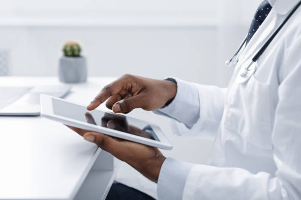 Cropped of black doctor using digital tablet at workplace