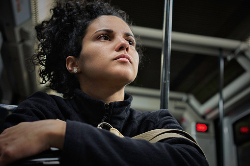 Pensive Hispanic young woman with curly hair traveling in the subway