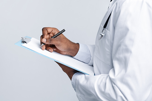 Cropped of african american doctor filling up medical form, side view, white studio background