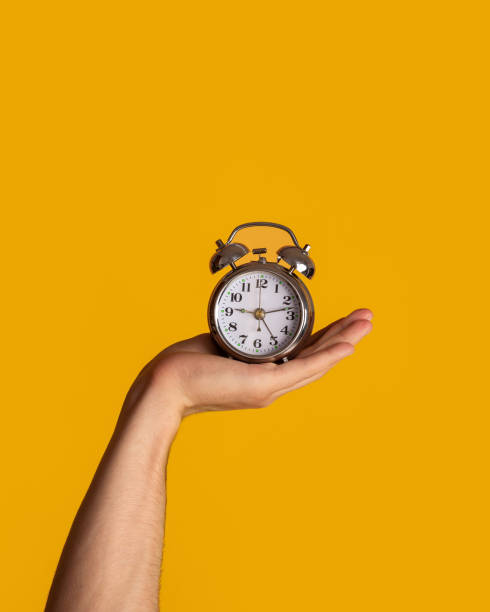 istock Time management. Young guy holding alarm clock on orange background, close up 1222193106