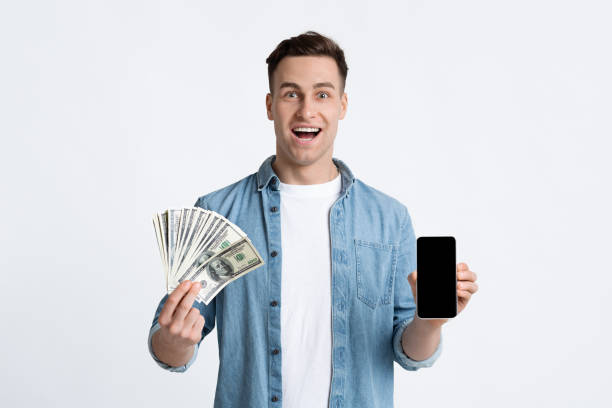 istock Guy holds dollars and smartphone with blank screen 1222194177