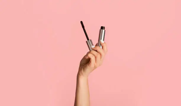 Photo of Beauty and makeup. Young girl holding mascara on pink background, close up