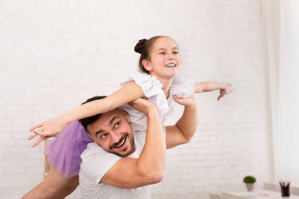 istock Father holding his cute daughter like plane at home 1222196721
