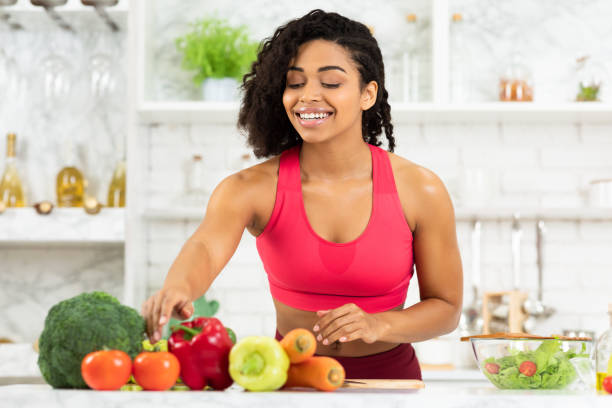 feliz joven mujer negra preparando ensalada de verduras - sistema inmune humano fotografías e imágenes de stock