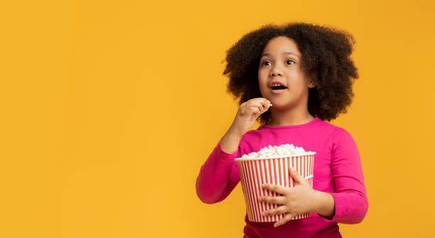 menina africana animada comendo pipoca e olhando para longe com espanto - child excitement awe fun - fotografias e filmes do acervo