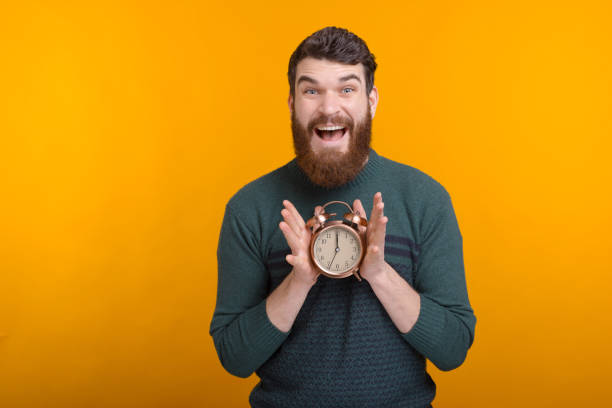 istock Excited man is showing an alarm clock looking at the camera on yellow background. 1222199065