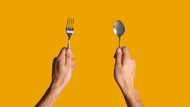 istock Unrecognizable millennial guy holding spoon and fork on orange background, close up. Panorama 1222200247