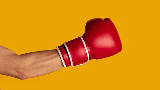 Closeup of strong sportsman wearing boxing glove on orange background, panorama