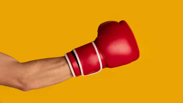 Photo of Closeup of sportsman wearing boxing glove on orange background, panorama