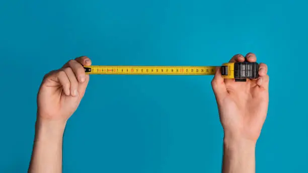 Photo of House renovation. Unrecognizable repairman holding tape measure on blue background, closeup. Panorama