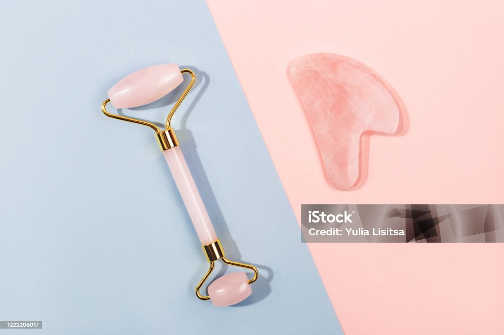 Pink jade roller and gua sha tool on pastel background. Pink jade roller and gua sha tool on pastel background. Trendy beauty tool. Minimal composition. Gua Sha Stock Photo