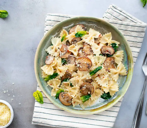 farfalle pasta with mushrooms and spinach, served in a ceramic plate. Gray background. Mediterranean cuisine. top view.