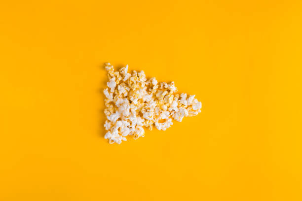Popcorn in the shape of play button on yellow background. Flat lay banner, top view. To go to the cinema concept. I like watching films.