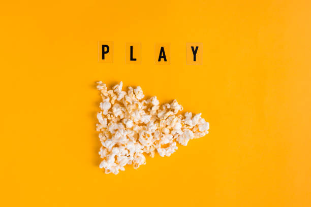 Popcorn in the shape of play button and text PLAY on yellow background. Flat lay banner, top view. To go to the cinema concept. I like watching films.