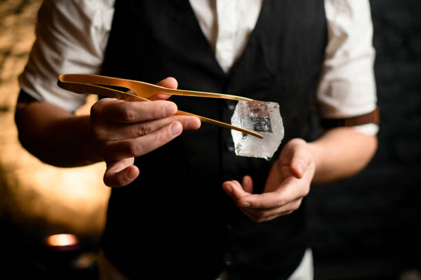 Close-up. Barman holding big cube of ice using tweezers. Close-up. Barman at bar accurate holding big cube of ice with tweezers in his hand. giant cube stock pictures, royalty-free photos & images